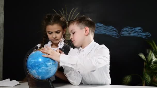 Concepto escolar. Los escolares se sientan en un escritorio jugando con un globo en él. Los niños se divierten apuntando a lugares al azar — Vídeos de Stock