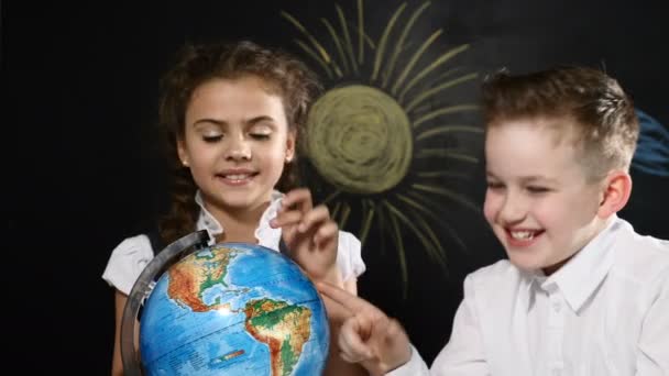 Travel concept. kids sit at a desk playing with a globe on it. Children have fun pointing at random places choosing a place to travel. — Stock Video