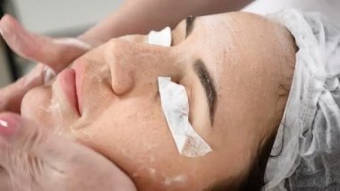 Genç kadın güzellik salonunda yordamlar almak güzel. Kanepede yatan genç güzel esmer kadın. Güzellik uzmanı yüz temizleyici köpük halinde femaale yüz ve boyun losyonları