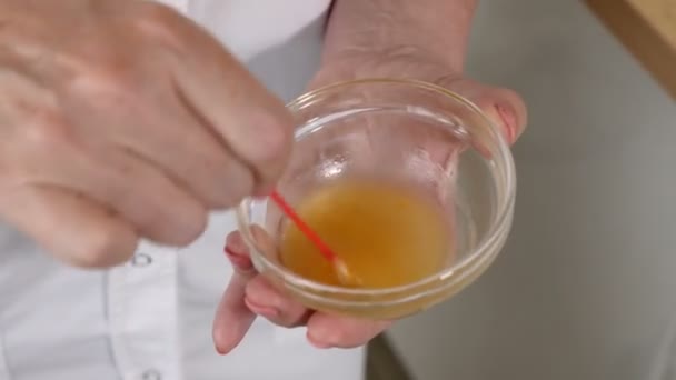 Centro de belleza. Beautician prepara mascarilla de belleza facial revolviendo los componentes en un recipiente de vidrio con un brote de algodón. De cerca. — Vídeo de stock