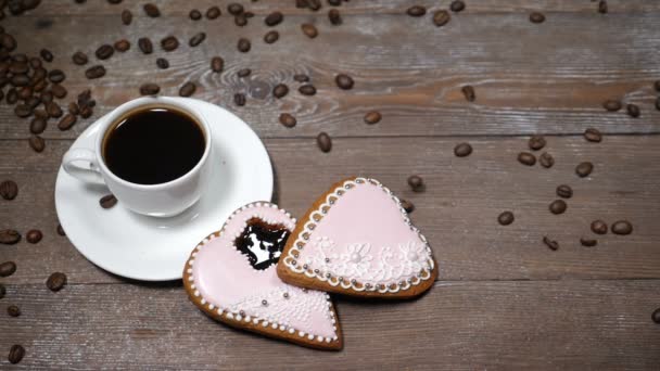 Voedsel-art. Goedemorgen concept. kopje koffie en 2 hartvormige gingersnaps zijn op houten achtergrond. Koffiebonen vallen naar beneden in slow motion — Stockvideo
