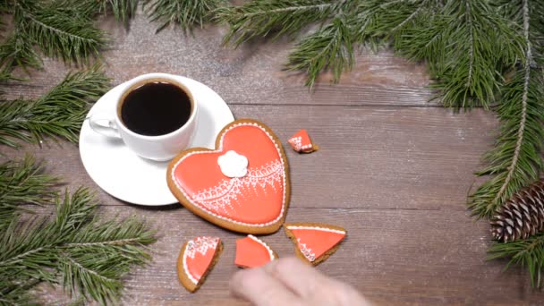 Food art.Broken heart. Fir tree, a cup of fresh-brewed coffee and heart-shaped gingersnaps placed on wooden background.one cookie is broken into pieces Top view.Female hands takes a piece. — Stock Video