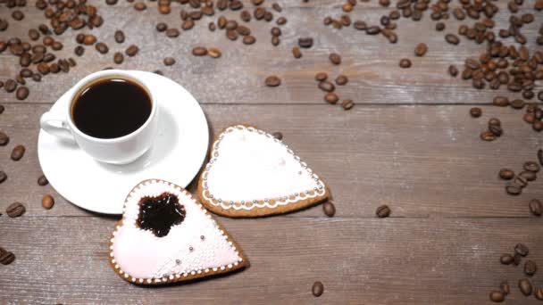 Искусство еды. Доброе утро. чашка кофе и 2 сердца форме gingersnaps на деревянном фоне. Кофейные зерна падают в замедленной съемке — стоковое видео