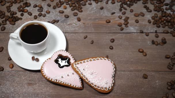 Arte de la comida. Buenos días concepto. taza de café y 2 encajes de jengibre en forma de corazón están sobre fondo de madera. Los granos de café caen en cámara lenta — Vídeos de Stock