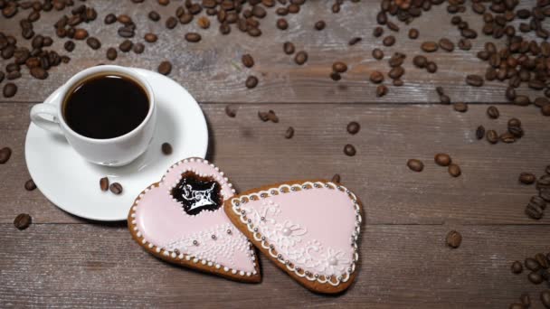 Arte alimentar. Bom dia, conceito. xícara de café e 2 gingersnaps em forma de coração estão no fundo de madeira. Grãos de café caem em câmera lenta — Vídeo de Stock