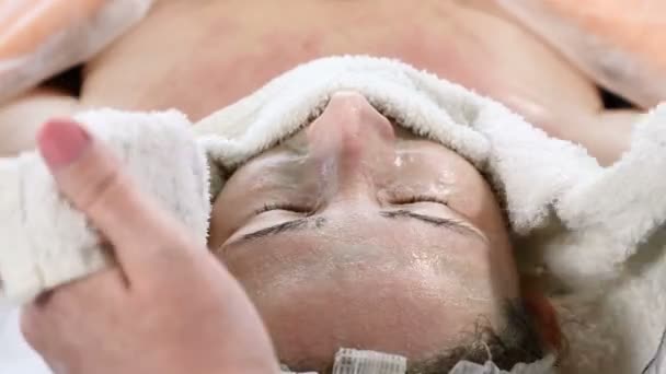 Giovane bella donna ottenere procedure in salone di bellezza. Giovane bella donna dai capelli scuri sdraiata sul divano. Estetista avvolge il viso femminile con un caldo asciugamano viso di pulizia — Video Stock