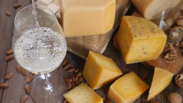 Arte de la comida. Diferentes tipos de queso bellamente dispuestos sobre fondo de madera. Vista superior. Se está vertiendo vino blanco en un vaso. Cámara extra lenta . — Vídeo de stock