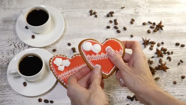 Voedsel-art. Gebroken hart concept. 2 kopjes koffie freshbrewed en 2 heartshaped peperkoek Cookies geplaatst op houten achtergrond met koffiebonen rond. Vrouwelijke handen nemen een cookie en breken — Stockvideo