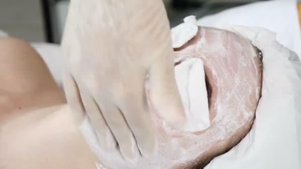 Clinique de santé. Jeune femme séduisante obtenir des soins du visage professionnel. Esthéticienne écarte le masque de crème faciale sur le visage avec les doigts. Les yeux sont fermés avec des tampons de coton — Video