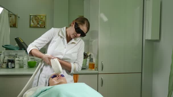 Skin care. Woman with glasses on eyes getting photo rejuvenation procedure in a beauty salon. Beautician performing facial procedure. Shot in 4k — Stock Video