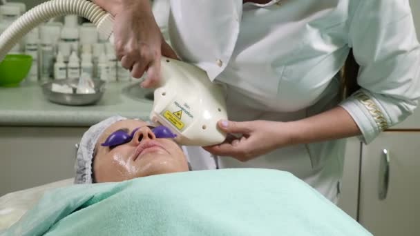 Cuidado de la piel. Mujer con gafas en los ojos recibiendo procedimiento de foto rejuvenecimiento en un salón de belleza. Esteticista realizando procedimiento facial. Disparo en 4k — Vídeos de Stock