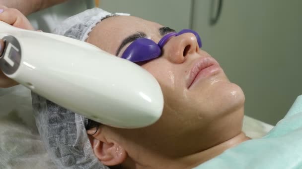 Hautpflege. Frau mit Brille auf Augen bekommt Foto-Verjüngungskur in einem Schönheitssalon. Kosmetikerin, die Gesichtsbehandlung durchführt. Schuss in 4k — Stockvideo