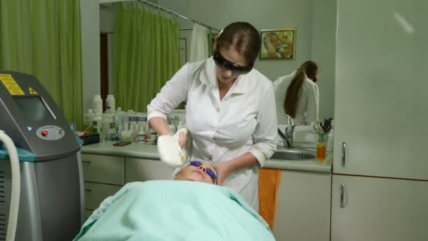 Hautpflege. Frau mit Brille auf Augen bekommt Foto-Verjüngungskur in einem Schönheitssalon. Kosmetikerin, die Gesichtsbehandlung durchführt. Schuss in 4k — Stockvideo