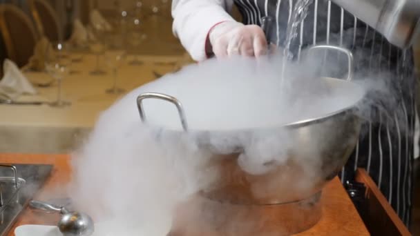 Cucinare nel ristorante. Una cuoca al lavoro. Proffessionale chef in guanti cucina dessert con ghiaccio secco. Lo chef versa l'acqua nella ciotola con ghiaccio secco. Rallentatore . — Video Stock