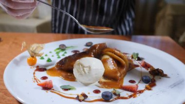 Restoran tatlı yemek kavramı. Son dokunuş kavramı. Şef eldiven karamel sos ile dondurma ve çilek ile dekore edilmiş krep yemek üzerine dökülen