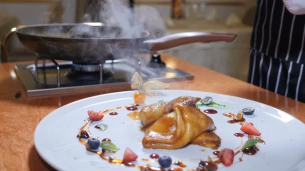 Essensausgabe. Nahaufnahme eines Küchenchefs, der Pfannkuchen im Flammenstil auf einem Teller serviert, der mit Beeren und Früchten dekoriert ist. Restaurantkonzept. Zeitlupe — Stockvideo