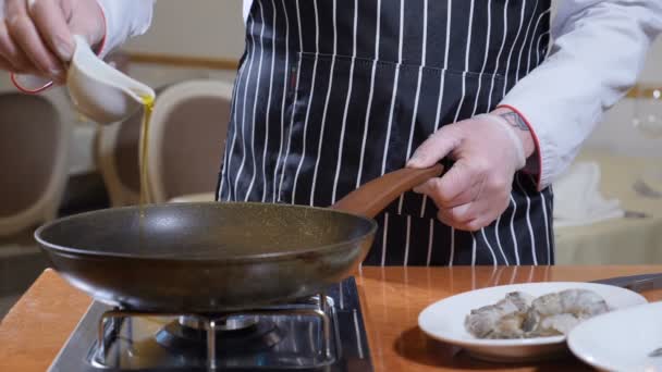 Cucina del ristorante. Lo chef in guanti versa olio d'oliva sulla padella per friggere gamberetti tigre flambestyle. Rallentatore — Video Stock