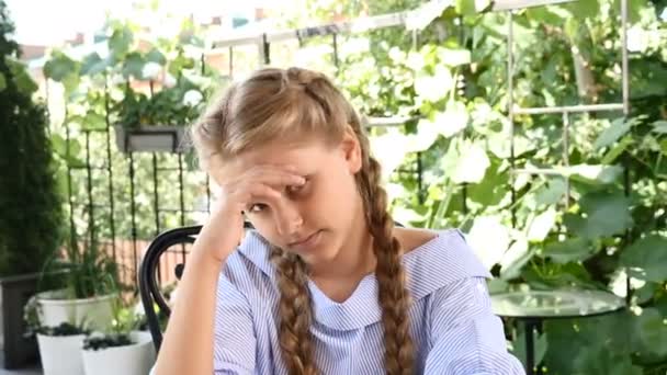 A criança ensolarada sorri. Feliz conceito de infância. Uma menina bonita senta-se em um café de rua à mesa, desfrutando de férias de verão e tempo livre — Vídeo de Stock