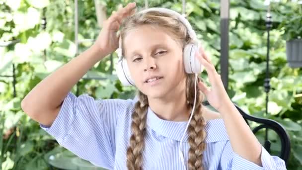 Retrato de una chica guapa sentada en un café de la calle con un cuaderno en la mesa y auriculares en la cabeza. escuchar música, disfrutar de las vacaciones de verano. Tiempo libre antes de la escuela — Vídeos de Stock