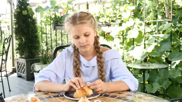 A comer fora. Menina adorável bonito comer croissant e mostrando gesto de aprovação. O polegar está levantado. Infância feliz . — Vídeo de Stock