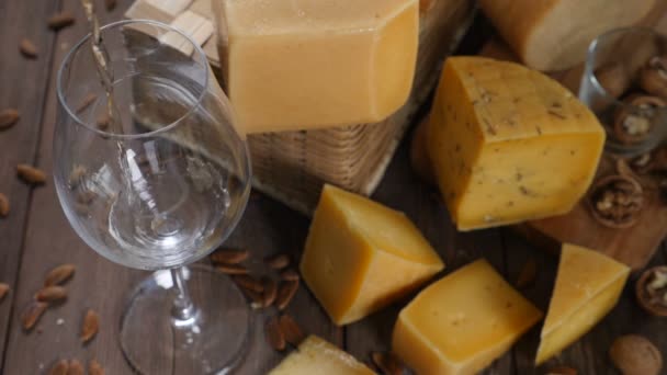 Cheese and wine. Variety of cheese placed on wooden background. wine is being poured into wine glass in slow motion — Stock Video