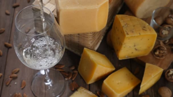 Τυρί και κρασί. Ποικιλία τυριών τοποθετείται σε ξύλινα φόντο. κρασί να χύνεται από ποτήρια κρασιού σε αργή κίνηση — Αρχείο Βίντεο