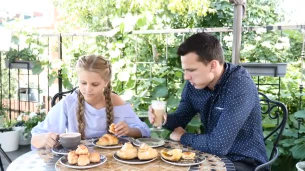 Eating out. handsome young man and little cute girl are together having breakfast in open terrace of restaurant. Delicious homebaked pastry and cups with hot chocolate and coffee are on table — Stock Video