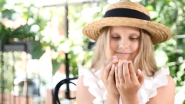 At först ur fokus zooma i fokus. Porträtt av söta lilla flicka håller nybakat kaffe caked täckt med nötter. Tjej visar händer med tårta till kamera. 4k — Stockvideo