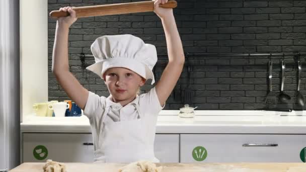 Симпатичный дошкольник в фартуке и шляпе шеф-повара, играющий со скалкой, развлекающейся. Кулинария это весело. 4 k — стоковое видео