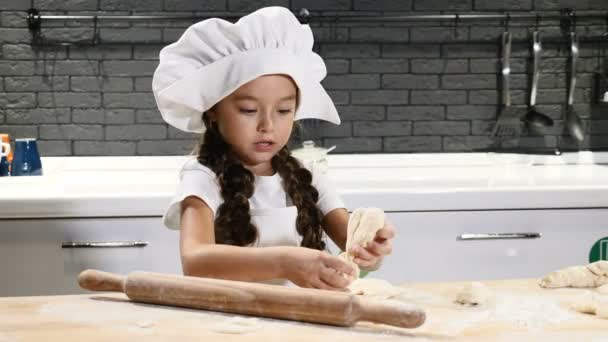 Kinderen koken. Klein meisje in de hoed van de chef-kok spelen met deeg en deegroller. Lachen met plezier in de keuken. 4k — Stockvideo