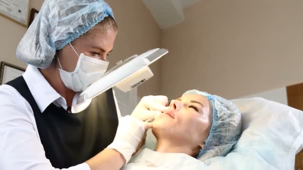 Концепция подтяжки лица. Женщина в медицинском центре красоты проходит процедуру по улучшению губ. Красавчик в перчатках делает инъекции красоты. 4k — стоковое видео