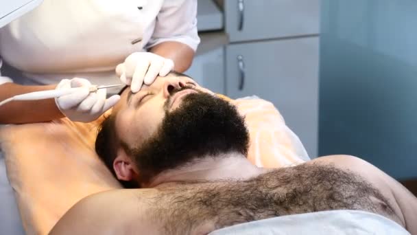 Brutal homme aux cheveux foncés obtient taupe médicale et papillomes procédure d'élimination dans le centre médical.Docteur enlève papillome de la paupière masculine. 4k — Video