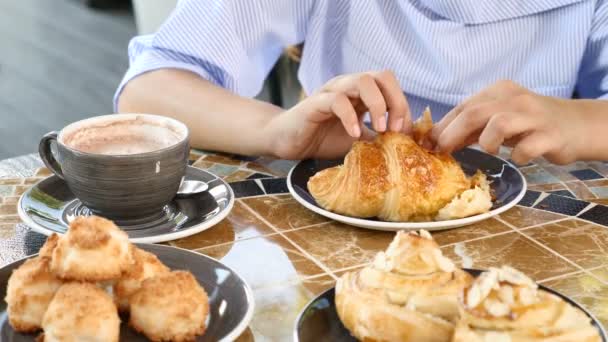 Close up de mãos femininas segurando um croissant e chocolate quente em um restaurante. 4k — Vídeo de Stock