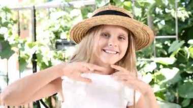 Yakın bir şekilde gülerek kameraya gülümseyen bir hasır şapka, küçük kız. Mutlu çocukluk kavramı. Yaz tatili. 4k