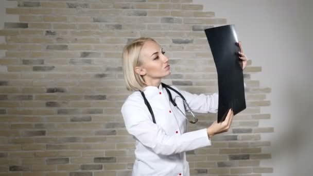 Médico loiro atraente feminino em vestido médico branco examinando raio-X na clínica de saúde. Conceito de saúde. 4k — Vídeo de Stock