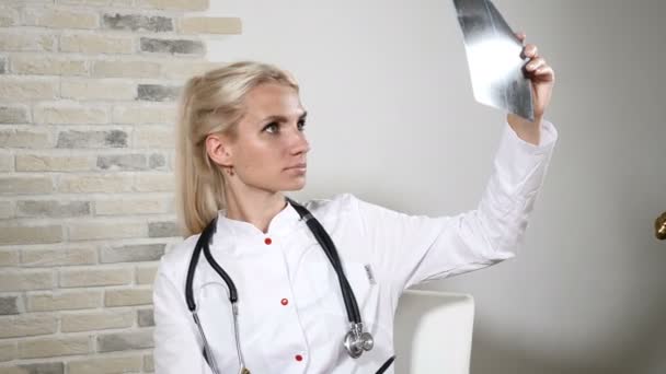 At health care clinic. Young cute female practitioner holding x-ray examining it in a hospital. Doctor radiologist. 4k — Stock Video