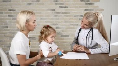 Genç kadın çocuk doktoru arkadaşlık güzel bir küçük kız ve annesi ile sağlık kliniğinde. Dost tıp kavramı. 4k