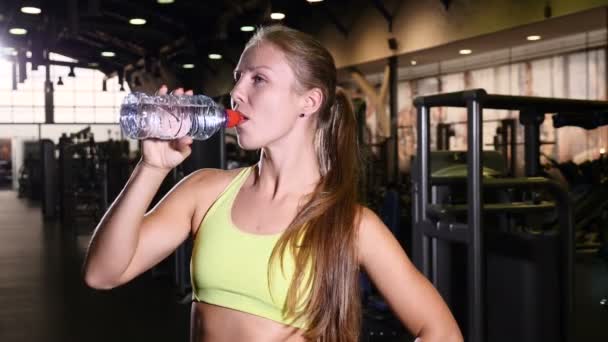 Egészséges élet fogalma. Sportos vékony nő ivóvíz tornateremben edzés után. A fiatal és gyönyörű sportoló mosolyogva. 4k — Stock videók