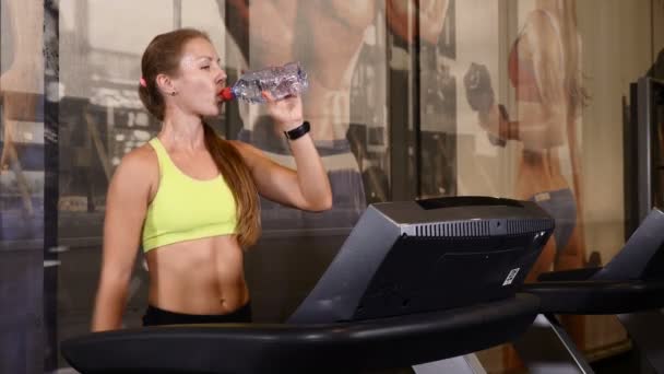 Exercices cardio sur la piste de marche dans la salle de gym. Jeune femme sportive faisant des exercices d'eau potable. 4k — Video