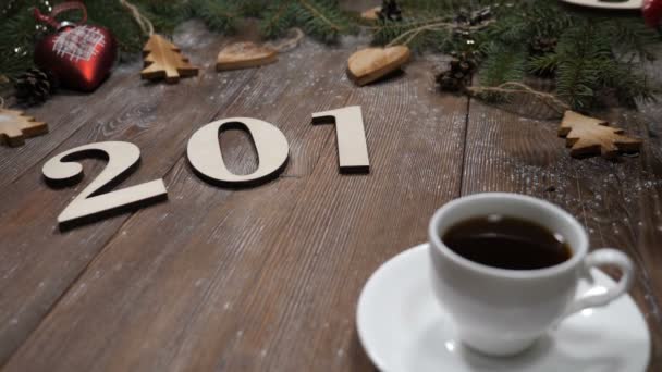 Merry Christmas and happy new year concept. 2019 wooden symbols and cup of coffee placed on background with fir tree branches and christmas toys. — Stock Video