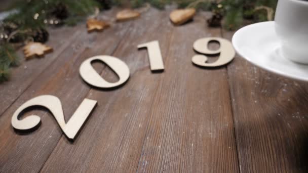 Buon Natale e felice anno nuovo concetto. 2019 simboli di legno, rami di pino e giocattoli di Natale su sfondo di legno. Le mani femminili mettono la tazza di caffè. Vista dall'alto — Video Stock