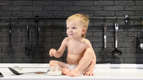 Малыш пробует сахар, когда его никто не видит. Голый милый младенец сидит на кухонном столе. 4k — стоковое видео
