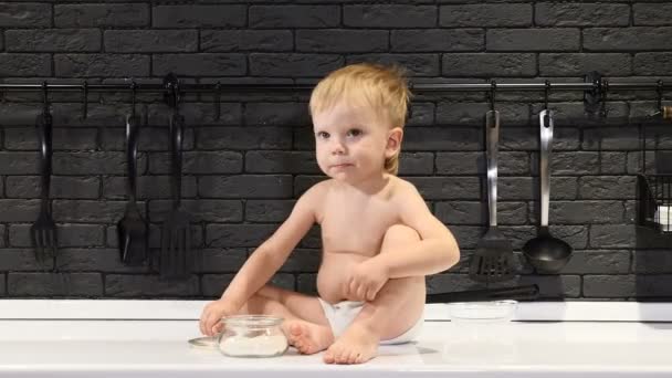 Очаровательный блондин сидит на кухонном столе и дегустирует сахар пальцем. 4 k — стоковое видео