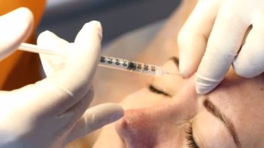 Modern kozmetik kavramı. Eldiven içinde dolgu ile şırınga tutarak Şevval özçelik güzellik. Enjeksiyonları alın ve glabellar kaşlarını hattı. Kadın yüz yordamı alır. 4k