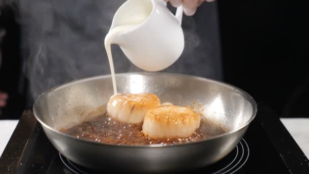 Kochen im Restaurant. Koch gießt Sahne auf Pfanne mit Jakobsmuscheln in Zeitlupe. Essenszubereitung. hd — Stockvideo