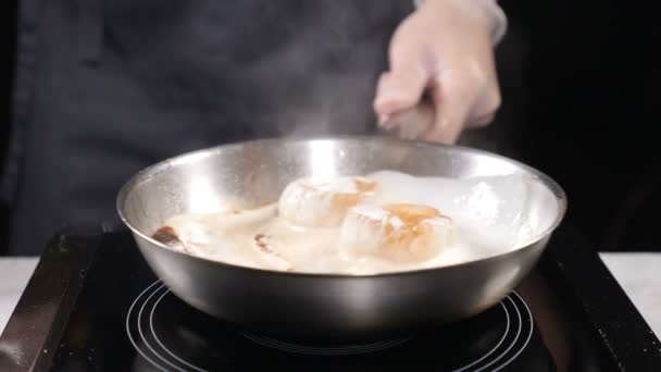 Cocinar en restaurante cocina profesional en guantes revolviendo sartén con vieiras hirviendo en salsa crema. En cámara lenta. hd — Vídeos de Stock