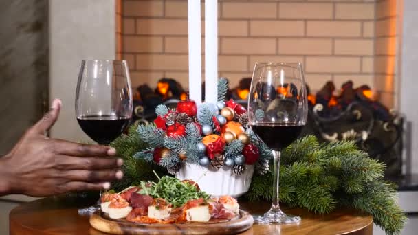 Vacaciones, año nuevo y concepto de celebración. Primer plano de las manos de un afro-americano tomando una copa con vino tinto en Navidad. Acogedora chimenea al fondo. 4k — Vídeo de stock