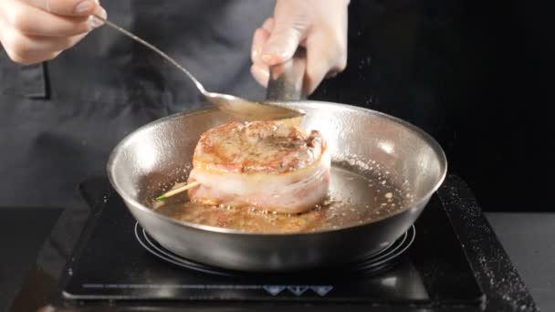 Стейк, мясо жарится в масла и смазки на сковороде. Шеф-повар наливает масло на стейк с ложкой. крупным планом в замедленном движении. Концепция нездоровой пищи. HD — стоковое видео