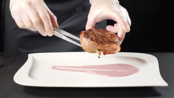 Kuchař, uvedení steak na talíři. Vaření v luxusní restauraci. Detailní záběr cheef hans míse. horké pečené maso steak je kladen na desku. HD — Stock video