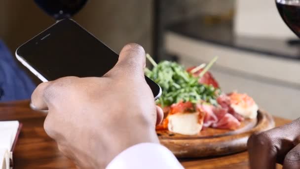 Крупный план афро-американской мужской руки в костюме с телефоном в ресторане. На столе тарелка с салатом. 4k — стоковое видео